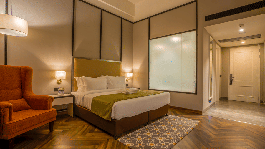 Guest room with king bed, orange armchair, herringbone wood floor and patterned rug at Polo Hotel, Agartala.