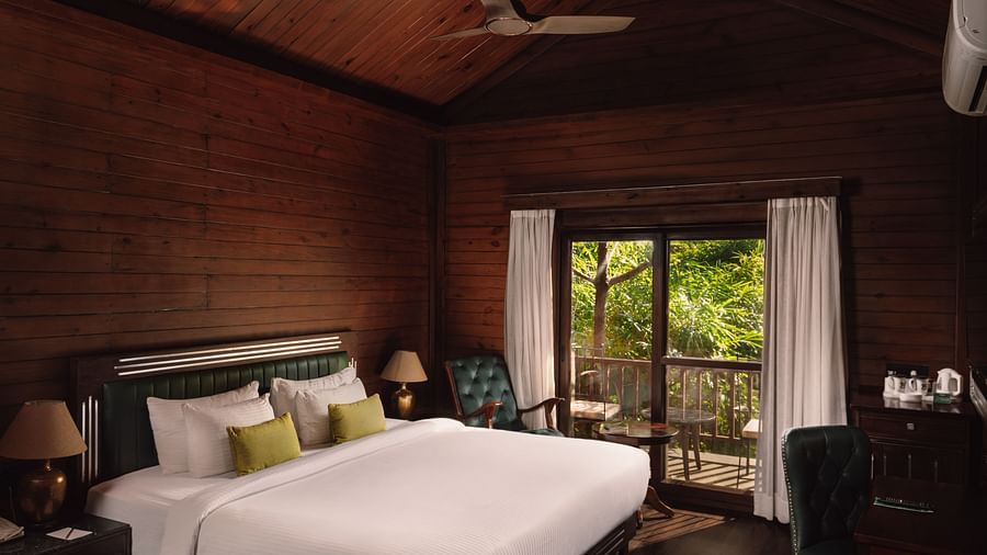 A corner view of Jungle Wood Bed Room  with a king sized bed, wooden walls, and bedside lamps and a spacious balcony.