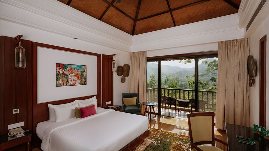 Corner view of the Luxury Villa bedroom at The Ananta, Udaipur, featuring a spacious balcony with scenic views, and a flat-screen TV, seating area with chair and a working desk.