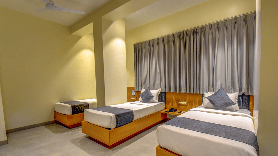 Delxue Triple Room at VITS Select Nashik Hotels & Resorts featuring 3 single beds next to each other under warm lighting against a curtained window