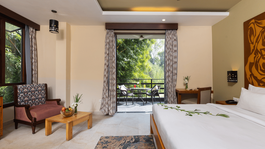  bedroom with a large bed, a seating area, and an open view to an outdoor patio  at The Golden Tusk, Jim Corbett