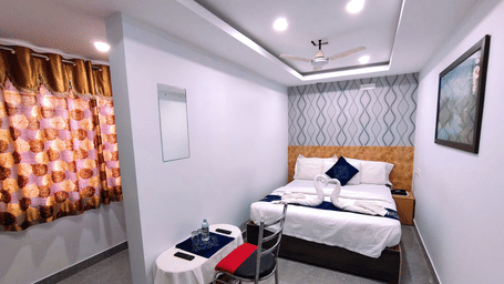 A brightly lit Economy Room at Housefinch Residency featuring a double bed against a patterned wall facing a work desk