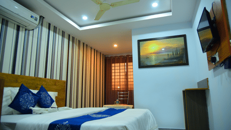 Premium Room at Housefinch Residency featuring double bed against a patterned wall with an air-conditioner over it facing the TV on the wall