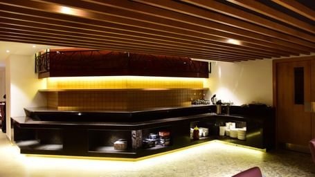 A long shot of the elegant restaurant and bar area at The Royal Comfort, showcasing a long bar with accent lighting and a cozy dining space with tables set for guests.