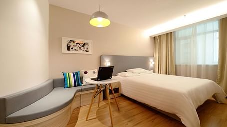 Bedroom with a white comforter, laptop, and a unique curved bench seat.