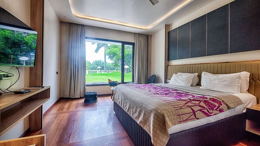 Deluxe Room at Crescent Resort, Sehore featuring a plush bed in front of a TV mounted on the wall and a sitting space next to the large window with the view of the nature outside