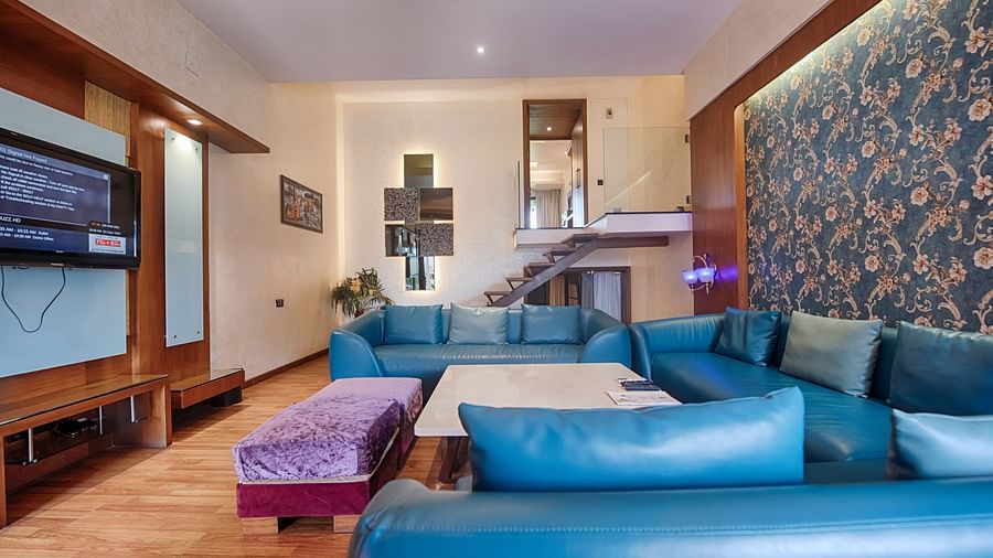 Living room of the Villa at Crescent Resort, Sehore featuring plush sofa set with a couple of ottomans surrounding the coffee table and a TV mounted on the wall opposite to them