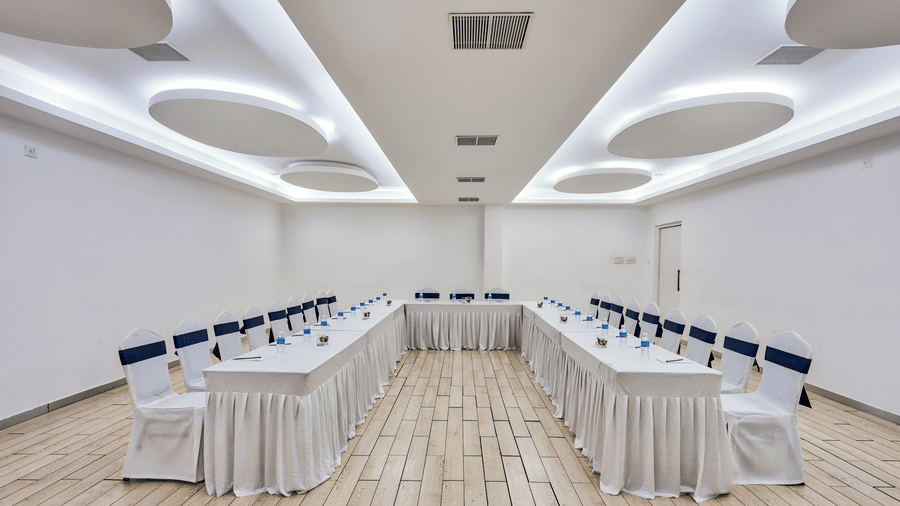 Conference hall setup with rows of tables and white chairs facing forward at Grande Bay Resort & Spa, Mamallapuram.