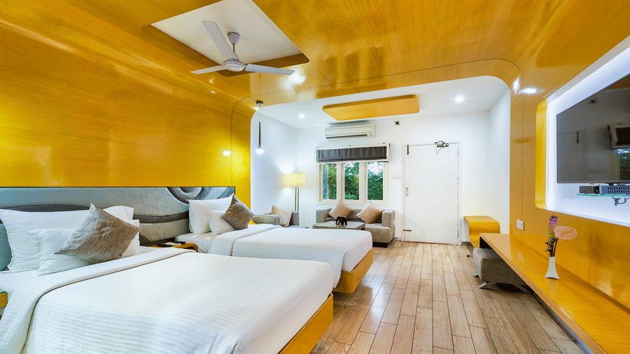 A room with twin beds with golden wall panel and white decor featuring a wall mounted television, and a seating area at Grande Bay Resort & Spa, Mamallapuram.