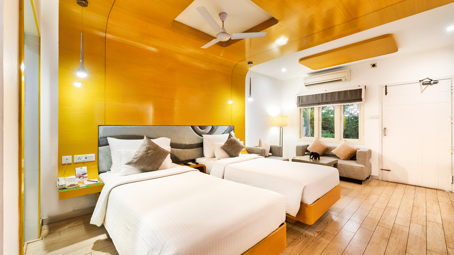A room with twin beds with golden panel wall and wooden flooring featuring a seating area at Grande Bay Resort & Spa, Mamallapuram.