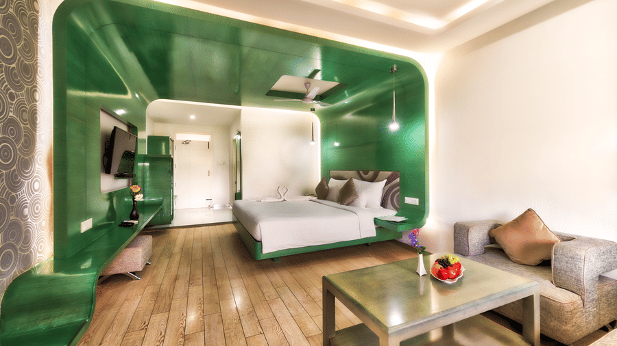 A room with king size bed, green glossy wall panel, and wooden furniture featuring a seating space at Grande Bay Resort & Spa, Mamallapuram.