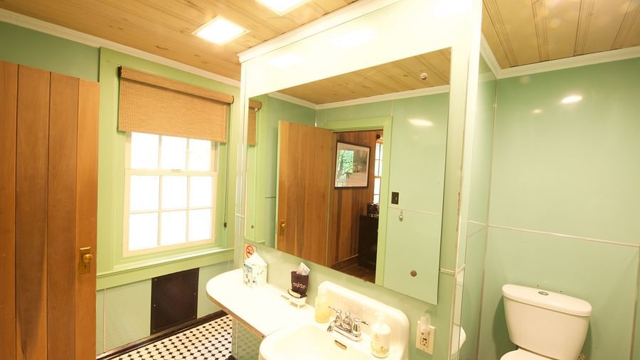 full view image of a bathroom featuring a wash basin with a wide mirror and a commode beside it with pastel green colored walls - Historic Tapoco Lodge