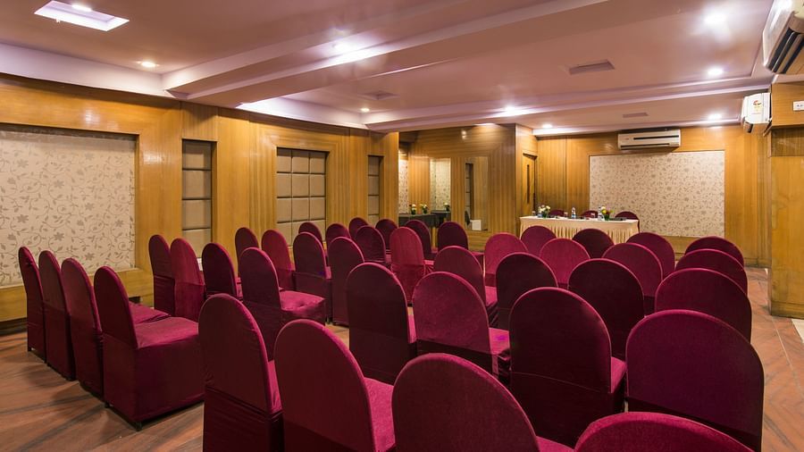 A hotel conference room with rows of red chairs facing a stage area - Lords Eco Inn Dahej