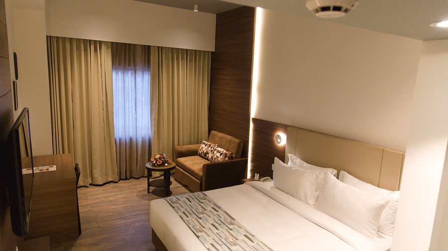 A comfortable hotel room at Lords Inn Udaipur features a double bed with white linens, a cozy armchair by the window, and modern furnishings.