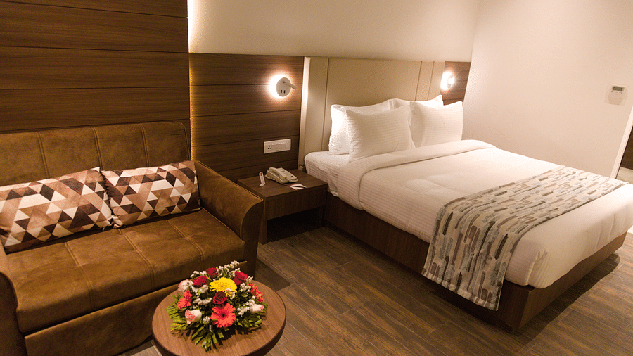 A well-appointed hotel room at Lords Inn Udaipur features a comfortable bed, a cozy sofa with patterned pillows, and a small round table with flowers.