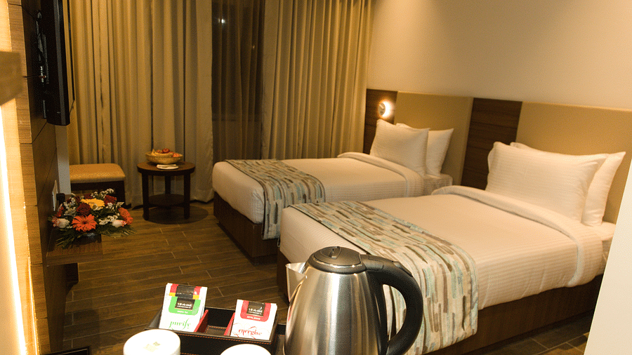 A hotel room at Lords Inn Udaipur offers two single beds with white linens, a kettle, cups, and tea bags on a counter.