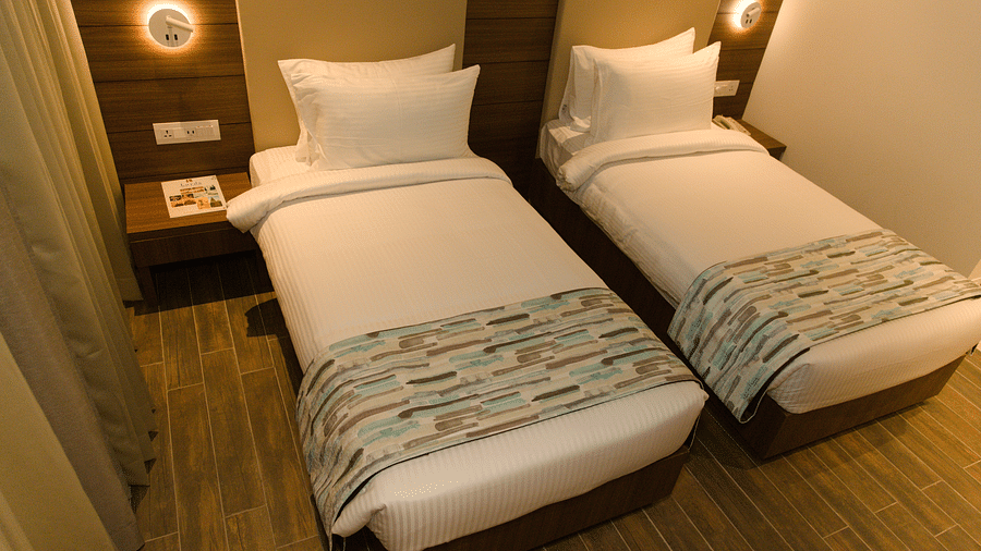 A hotel room at Lords Inn Udaipur features two single beds with white linens and patterned runners, flanked by illuminated wall sconces.
