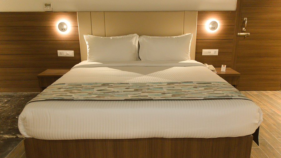 A neatly made bed with white linens and a patterned runner is centered between two illuminated wall sconces and bedside tables.