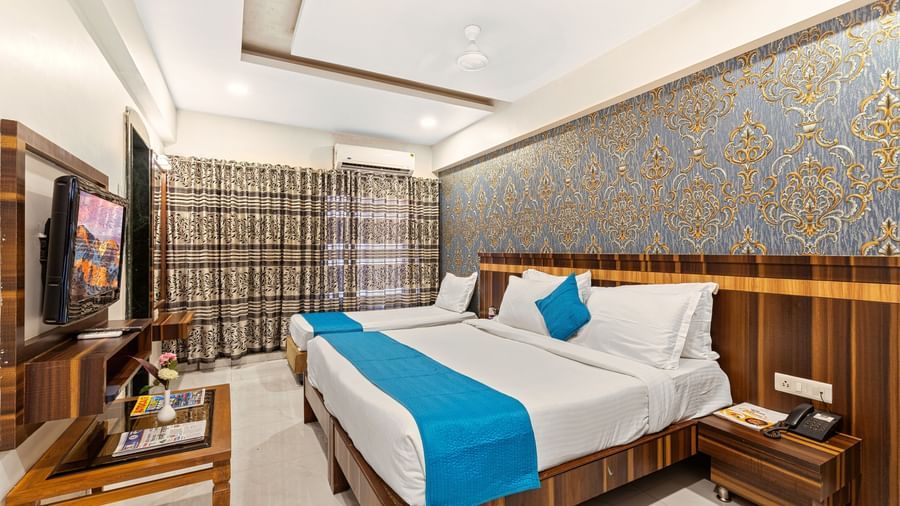 Spacious room at Mayur Retreat featuring a large double bed with turquoise throw and elegant blue wallpaper.