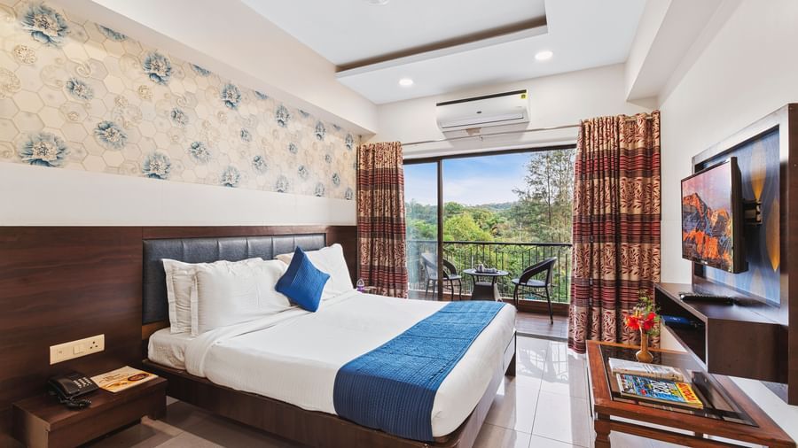 Bright and ventilated room at Mayur Retreat with a blue-themed bed, floral walls, and balcony garden view.