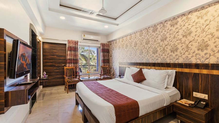 Warm-toned bedroom at Mayur Retreat with brown accents, floral wallpaper, and a scenic garden view.