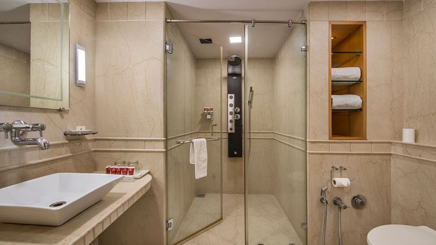 Modern bathroom with a glass-enclosed shower, a white sink, and neatly arranged towels - Lords Inn Vadodara