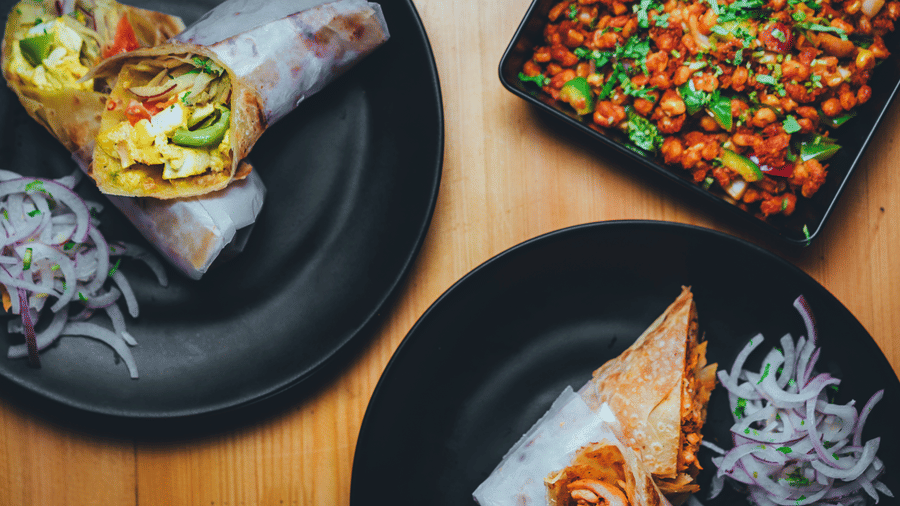 A display of 2 plate holds sliced wraps and onions, with a starter on the side nearby on a wooden table.
