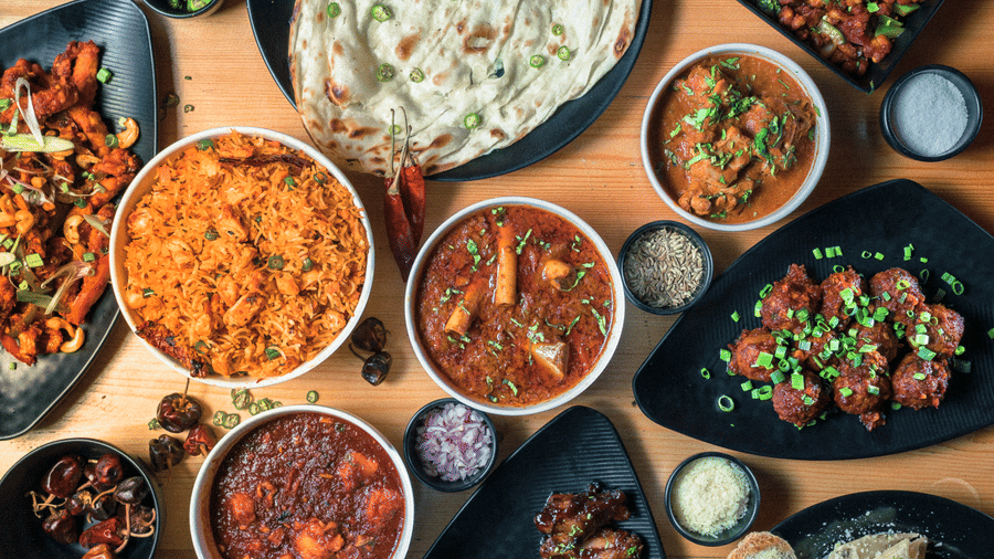 An overhead view shows a large wooden table covered with numerous dark bowls containing various Indian dishes at S Hotels, Chennai.
