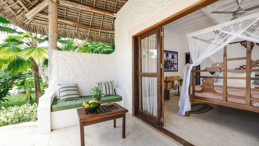 A private patio at a tropical resort with white walls, a thatched roof, and a view into a bedroom with a four-poster bed - Shooting Star Boutique Hotel.