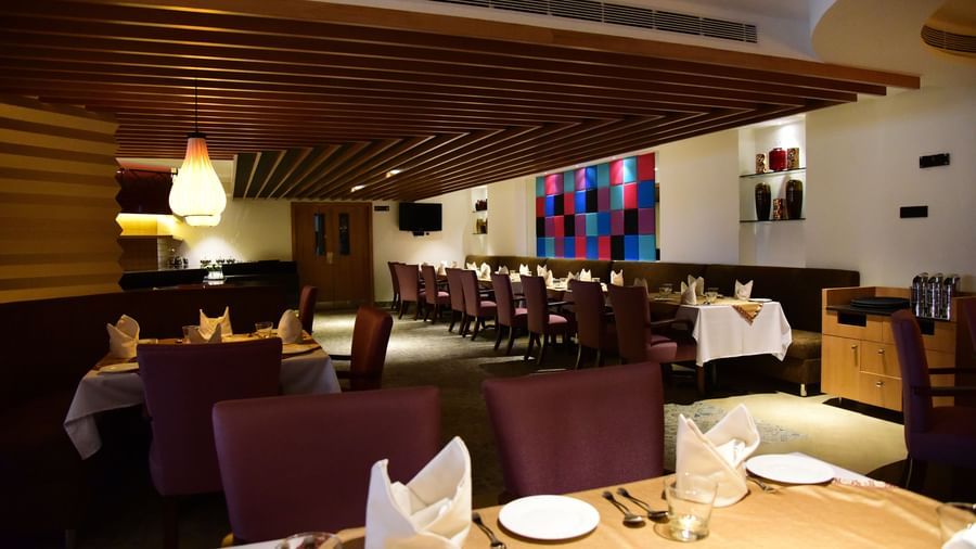 A side-angle shot of a hotel restaurant at The Royal Comfort, with elegant lighting, tables set for dinner, and a warm atmosphere.