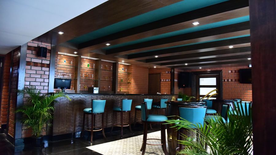 A vibrant hotel bar at The Royal Comfort, showcasing a brick-and-wood bar with bright blue-green barstools and a warm, inviting ambiance.