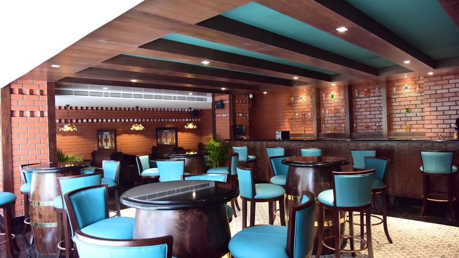 A close-up of the bar area at The Royal Comfort, with wooden rafters on the ceiling and a focus on the blue-green seating and intricate lighting fixtures.