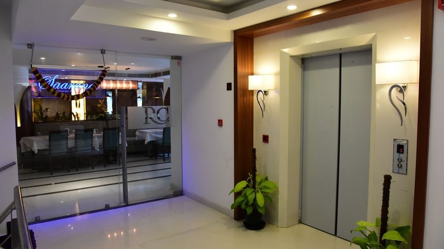 A sleek, modern elevator lobby at The Royal Comfort, with a metallic elevator door and glowing blue lights beneath a wooden ceiling panel.