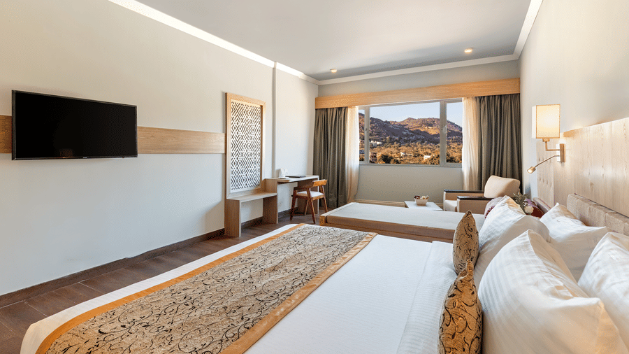 A close-up shot of a bed with a patterned runner on it and a tv mounted on the wall - Via Lakhela Resort & Spa, Kumbhalgarh
