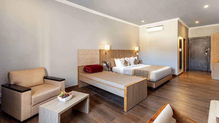 A well-lit hotel room with two beds, a beige armchair beside it and a small coffee table with fruits kept on it - Via Lakhela Resort & Spa, Kumbhalgarh