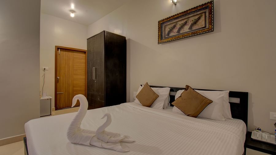 Swans made with towels on a huge bed, a cupboard, side table, a wall art and wooden door | Superior Room | Woodstock Resorts, Coorg