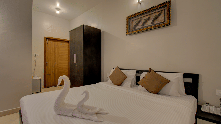 Swans made with towels on a huge bed, a cupboard, side table, a wall art and wooden door | Superior Room | Woodstock Resorts, Coorg