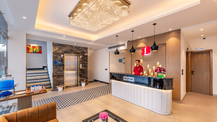 A grand reception area with a front desk and a staff member featuring marble floor, marble accent wall, pendant lights and a chandelier and a lift at Lords Eco Inn Dehradun.