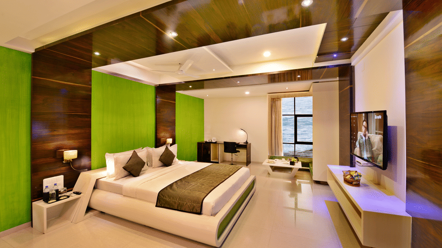 A contemporary hotel suite with a king size bed, green accent wall, and city view.