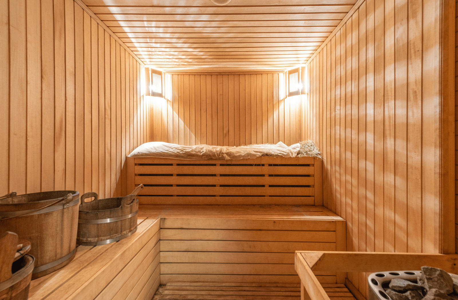 A wooden sauna room with two warm lights mounted in the corner of the ceilings.