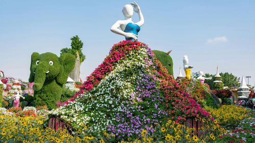 A colourful floral arrangement depicting a woman in a dress, surrounded by other flower arrangements at an outdoor show.