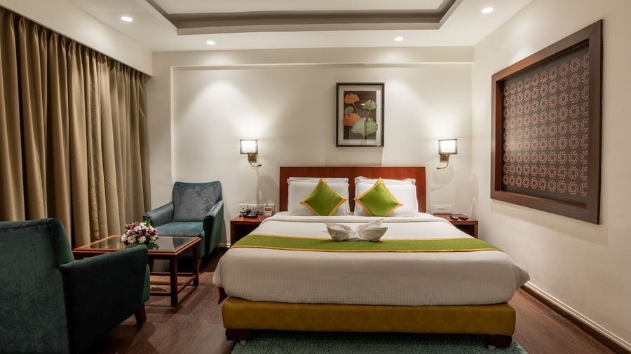 Well-lit room with king size bed, seating area, and framed artwork at Hotel Royal Regency Chennai