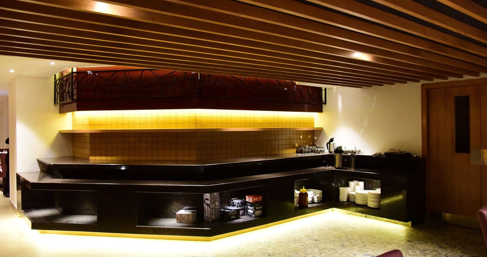 A long shot of the elegant restaurant and bar area at The Royal Comfort, showcasing a long bar with accent lighting and a cosy dining space with tables set for guests.