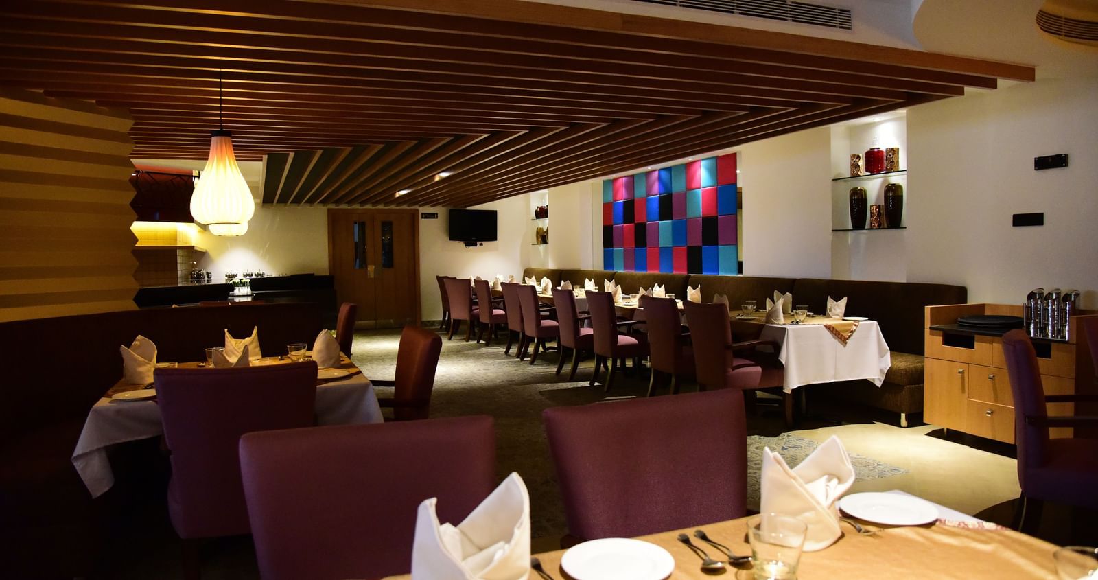 A side-angle shot of a hotel restaurant at The Royal Comfort, with elegant lighting, tables set for dinner, and a warm atmosphere.