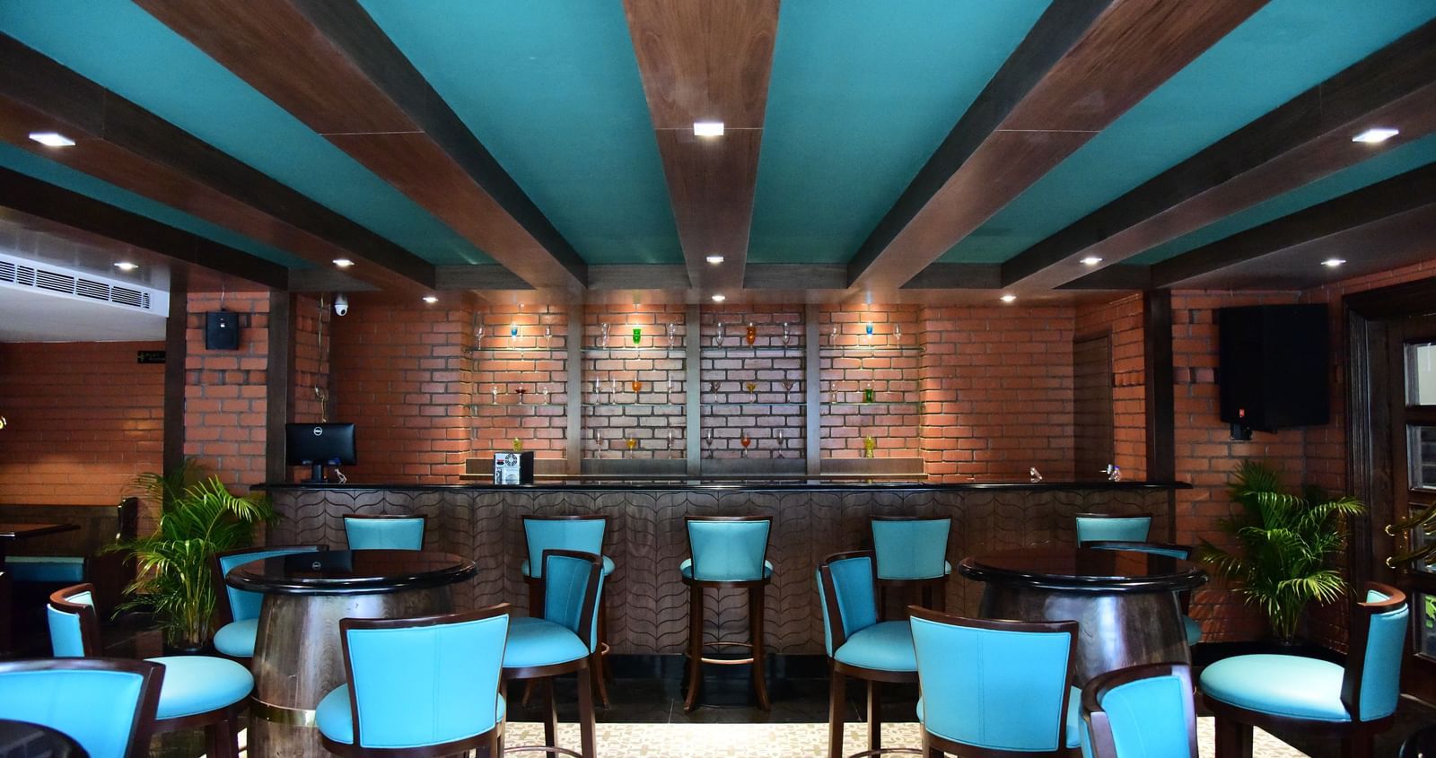Another view of the bar at The Royal Comfort, highlighting the long wooden bar top, the brick wall behind it, and the stylish blue-green chairs.