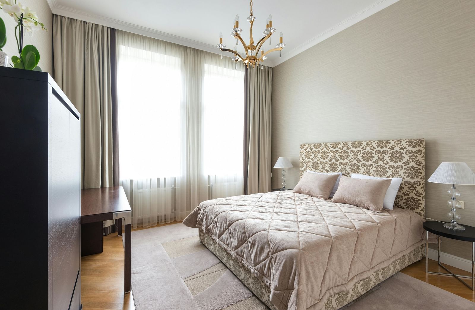 A bedroom features a patterned bedspread, neutral walls, and a chandelier.