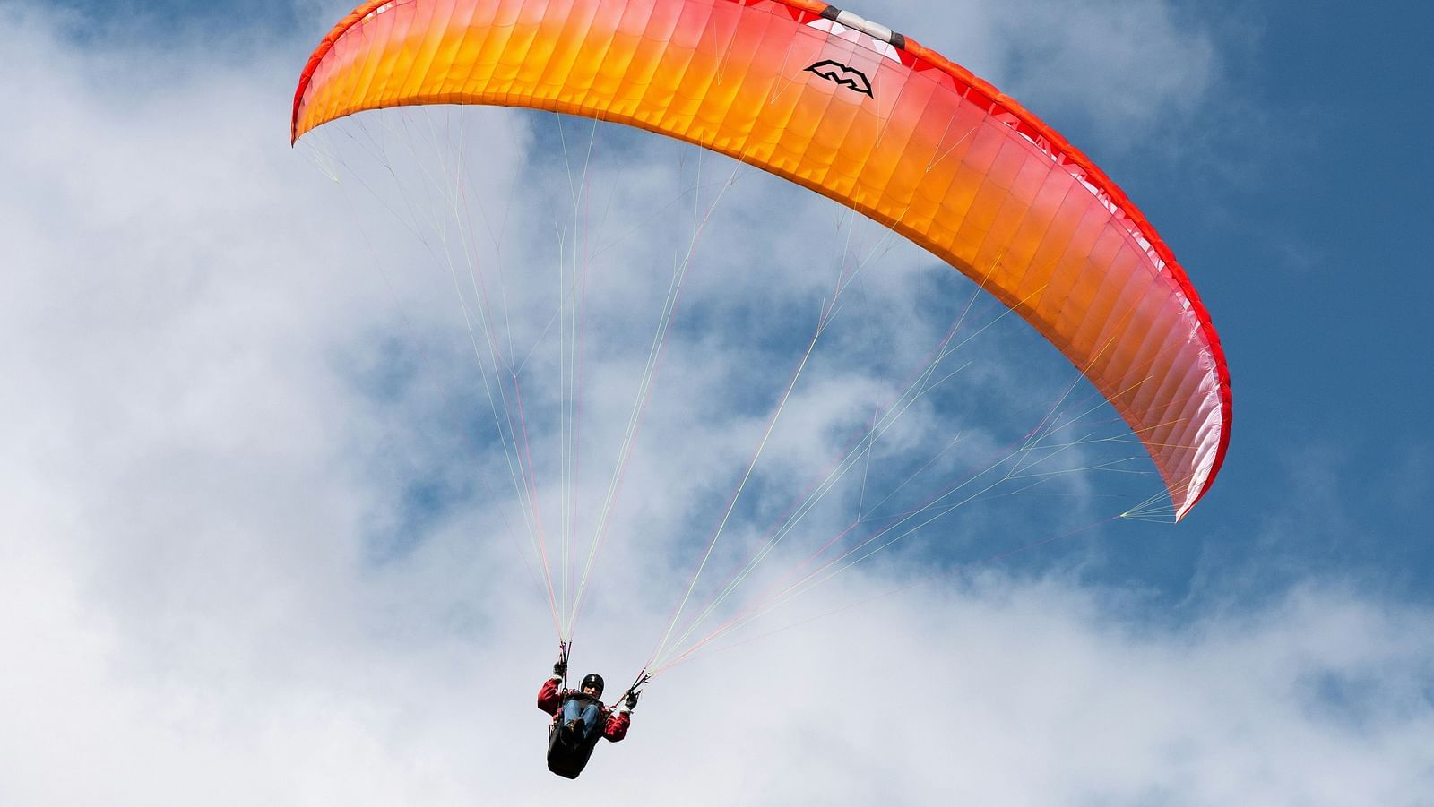 a person paragliding with a an orange parachute and blue sky in the background.