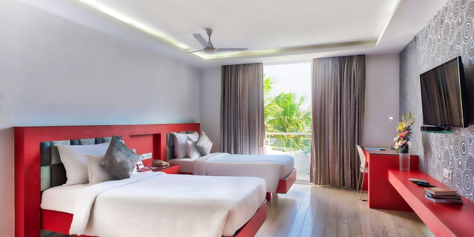 A modern hotel bedroom with a white bed, red frame, and a large window with white curtains | Grande Chalet | Grande Bay Resort & Spa, Mamallapuram