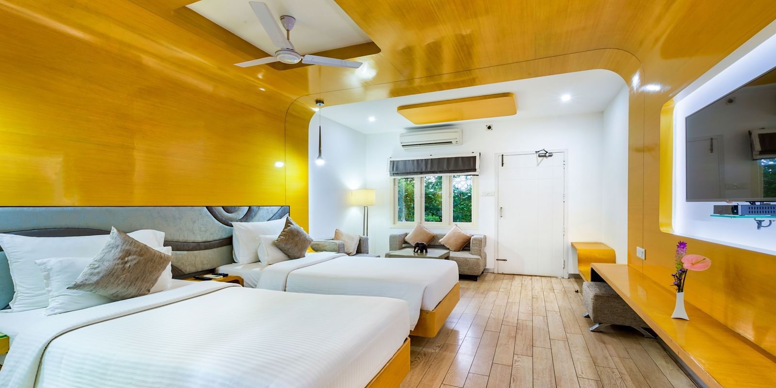 A room with twin beds with golden wall panel and white decor featuring a wall mounted television and a seating area at Grande Bay Resort & Spa.