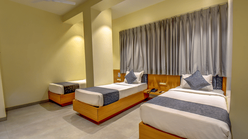 Deluxe Triple Room at VITS Select Nashik Hotels & Resorts featuring 3 single beds next to each other under warm lighting against a curtained window.